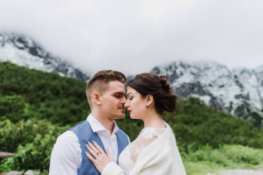 Güzel gelin ve damat dağlarda bir göl kenarında kucaklaşıyorlar. Gelin ve damat dağlarda.