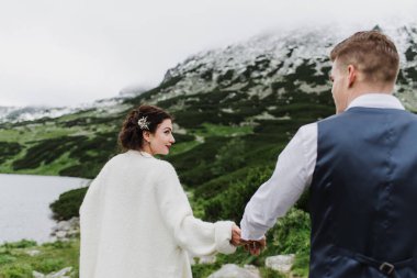 Güzel gelin ve damat göl kenarındaki dağlarda yürüyorlar..