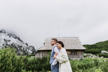 Güzel gelin ve damat dağlardaki ahşap bir evin yanında kucaklaşıyorlar..