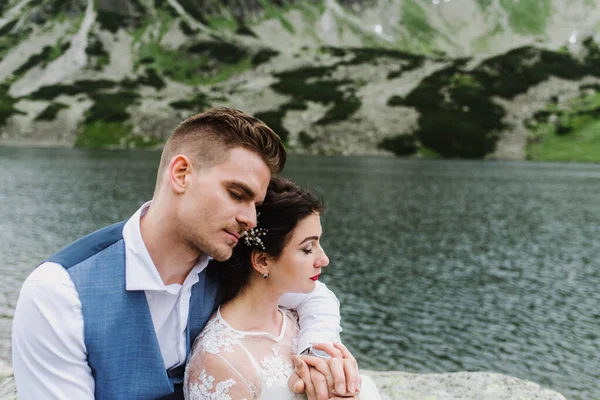 美丽的新娘和新郎在湖边的山上拥抱和亲吻 — 图库照片
