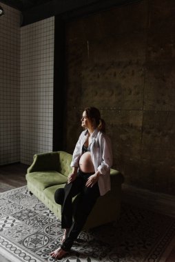 İç çamaşırlı hamile bir kadın ve stüdyodaki kanepede beyaz bir gömlek. Beyaz gömlekli hamile bir kadın salıncakta sallanıyor..