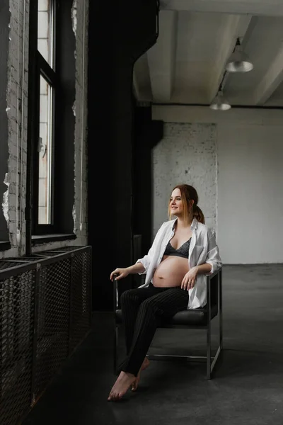 穿着内裤和白衬衫的年轻孕妇站在演播室窗前 — 图库照片