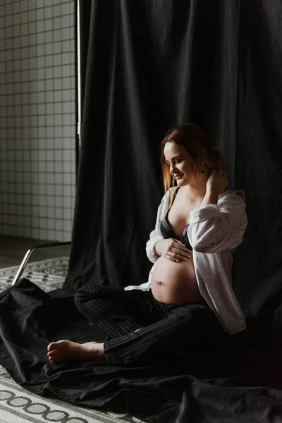 工作室里穿着内衣和白衬衫的年轻孕妇接近面料背景 — 图库照片