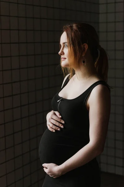 一个穿着黑色衣服的年轻孕妇站在窗边 — 图库照片