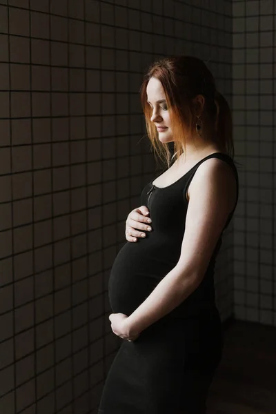一个穿着黑色衣服的年轻孕妇站在窗边 — 图库照片