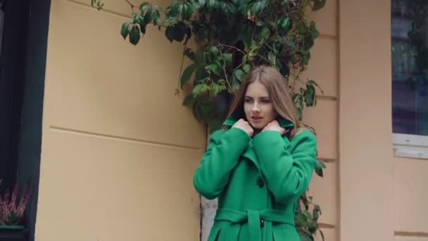 Стильная девушка в зеленом пальто позирует перед камерой 4K — стоковое видео