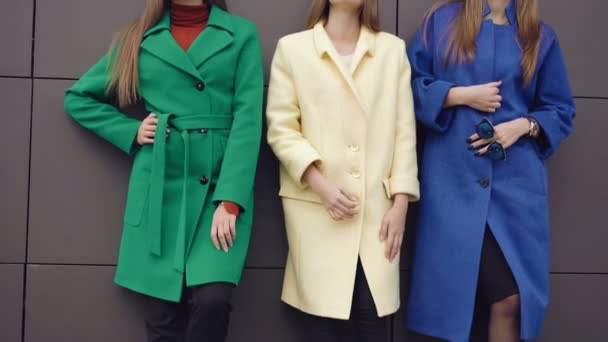 Trzy modele modne pozowanie na kamery w płaszcze w pobliżu ściany 4k — Wideo stockowe