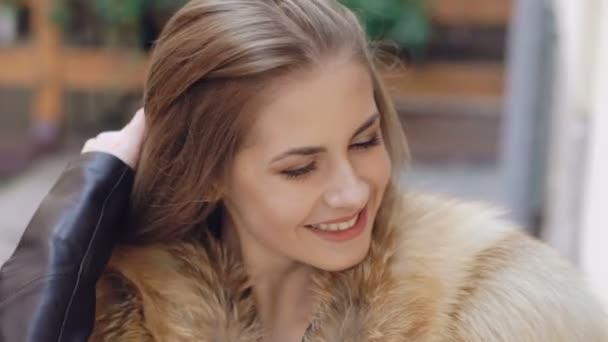Detailní záběr roztomilé dívky s úsměvem v chlupatý kabátek na ulici. Zpomalený pohyb — Stock video