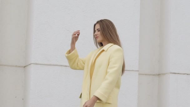 Ragazza carina con i capelli lunghi in posa cappotto sullo sfondo. Lentamente. — Video Stock