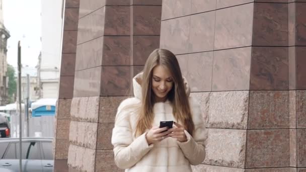 Menina feliz andando, usando o telefone e sorrindo perto do escritório. Devagar. — Vídeo de Stock