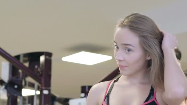 Chica bonita tocando el pelo y sonriendo a la cámara en el gimnasio. Despacio. — Vídeo de stock