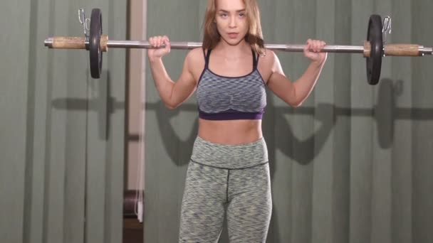 The girl working out with a barbell with heavy weights on her shoulders. Slowly — Stock Video