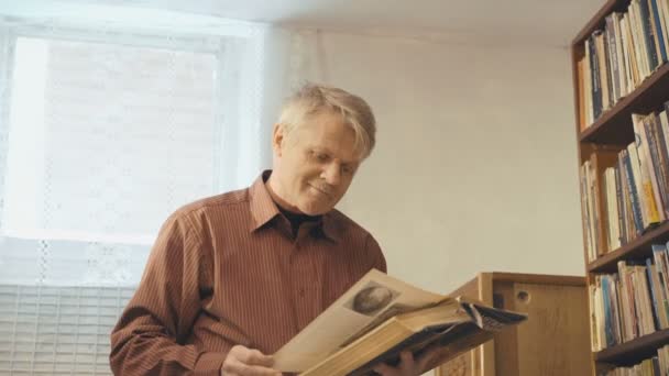 Старик смотрит в книгу и улыбается в камеру 4k — стоковое видео