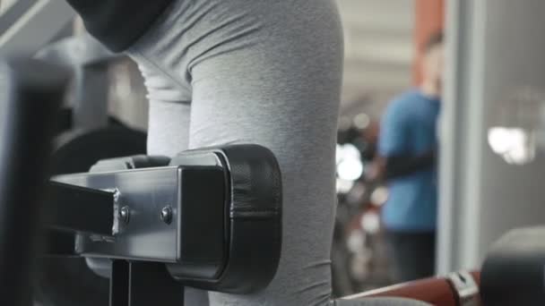 La chica haciendo ejercicio con el simulador para los músculos de las piernas y las nalgas en el gimnasio — Vídeos de Stock