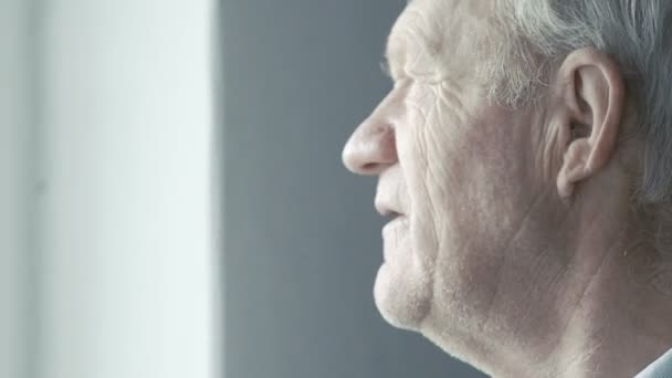 Old grandfather looking at the window and smiling at camera — Stock Video