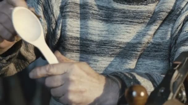 Portrait of old wrinkled carpenter hews wooden spoon and smiling at camera — Stock Video