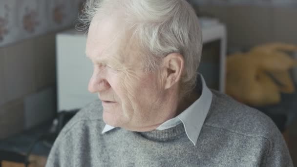 Старый грустный дедушка смотрит в окно и камеру 4K — стоковое видео