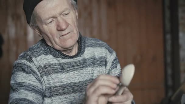 Cansado velho homem enrugado cortando sua colher de madeira artesanal e sorrindo para a câmera 4K — Vídeo de Stock