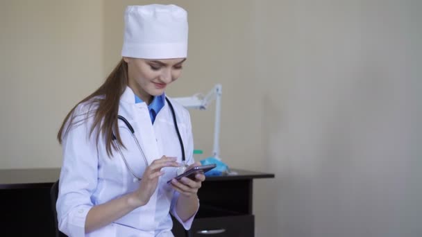 Jovem médica sentada com smartphone no hospital — Vídeo de Stock