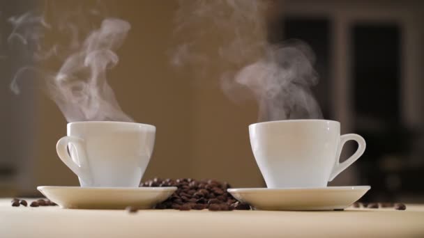 Duas xícaras brancas de café delicioso na mesa com grãos torrados em 4K — Vídeo de Stock