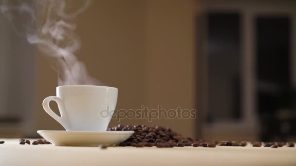 Uma xícara branca de café evaporando na mesa com grãos torrados em 4K — Vídeo de Stock