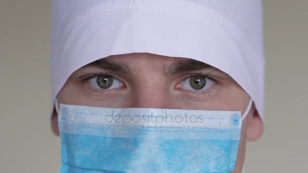 Egy férfi orvosok arc, öltözött a sebészeti maszk, nézi a kamera közelről — Stock videók