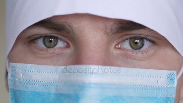 Close up van een gezicht van de mannelijke chirurgen gekleed in een chirurgisch masker kijken camera — Stockvideo
