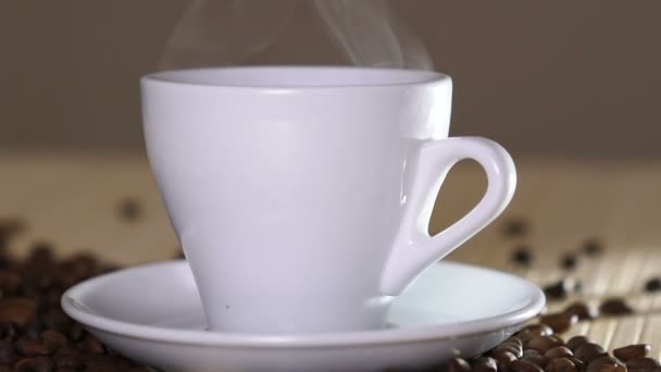 Primo piano di tazza bianca di caffè evaporante sul tavolo vicino ai fagioli tostati. Lentamente. — Video Stock