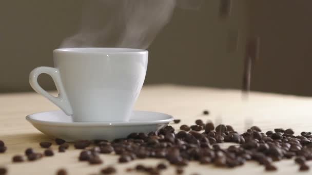 Primo piano di tazza bianca di caffè evaporante sul tavolo vicino ai fagioli tostati. Lentamente. — Video Stock