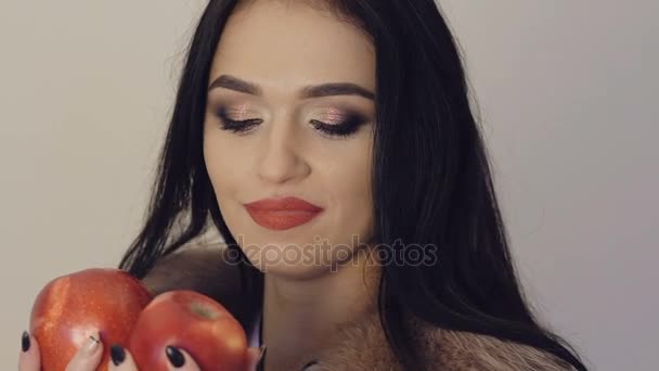 Chica apasionada en chaqueta peluda posando con dos manzanas rojas. Despacio. — Vídeos de Stock