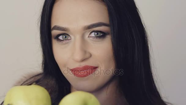 Chica bonita sonriendo y posando con dos grandes manzanas verdes en el fondo. Despacio. — Vídeo de stock