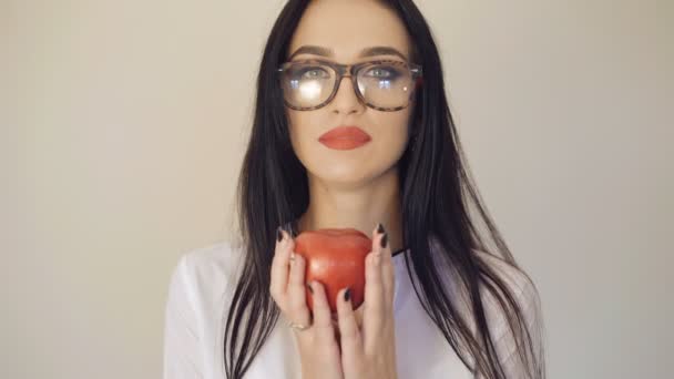 Милая брюнетка в очках держит и смотрит на красное яблоко в руках 4K — стоковое видео