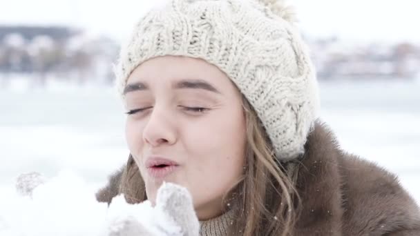 Όμορφο ευτυχισμένο κορίτσι φυσάει χιόνι εξωτερική. Σιγά-σιγά — Αρχείο Βίντεο
