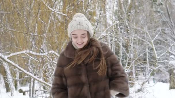Feliz chica sonriente caminando y mirando hacia atrás en el parque en un día nevado. Despacio. — Vídeo de stock