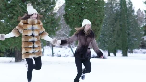 Две симпатичные девушки бегают по снегу в парке. Медленно. — стоковое видео