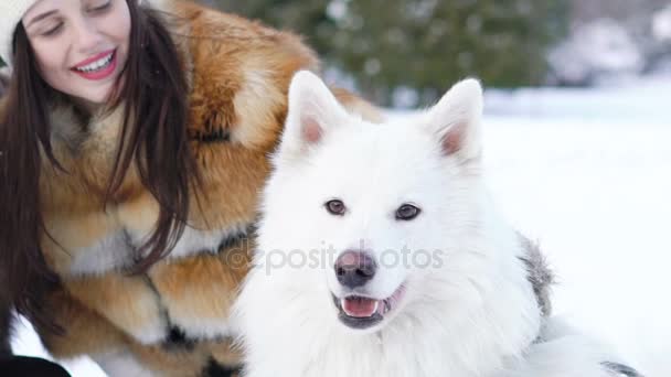 Dos chicas jugando con perro husky blanco en la nieve. Movimiento lento — Vídeos de Stock