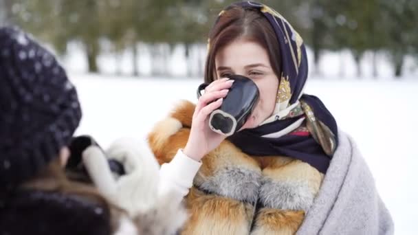 Dos chicas cubiertas de cuadros hablando, sonriendo y bebiendo té en el parque de invierno 4K — Vídeo de stock