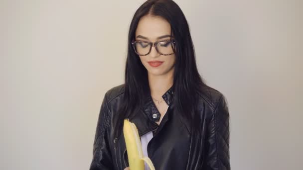 Cute girl in glasses peeling a big banana and smiling to camera 4K — Stock Video