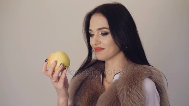 Niedliches Mädchen isst einen großen, saftigen Apfel, lächelt und flirtet im Hintergrund 4k — Stockvideo