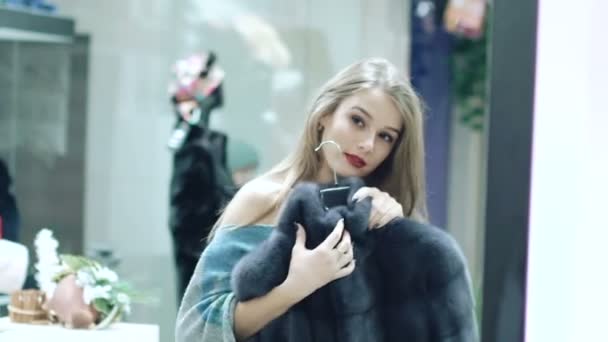 Красивая девушка выбирает шубу в магазине — стоковое видео