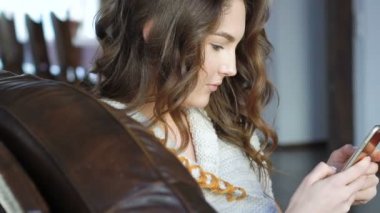 Deri kanepede rahatlatıcı ve cep telefonuyla güzel kız yakın çekim