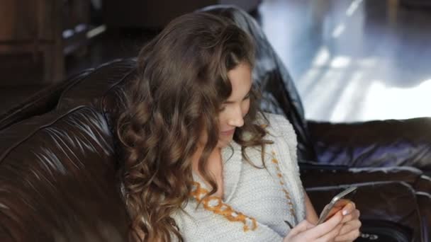 Close up de menina bonita relaxante no sofá de couro e usando telefone celular — Vídeo de Stock