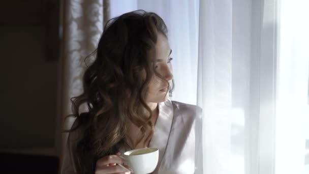 Chica guapa en la noche bebe una taza de café cerca de la ventana en 4K — Vídeo de stock