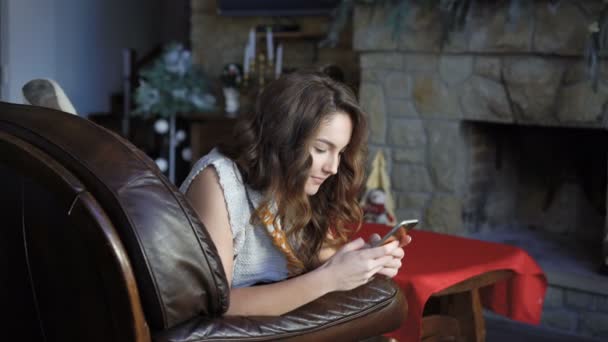 Красивая девушка отдыхает на кожаном диване и с помощью мобильного телефона 4K — стоковое видео