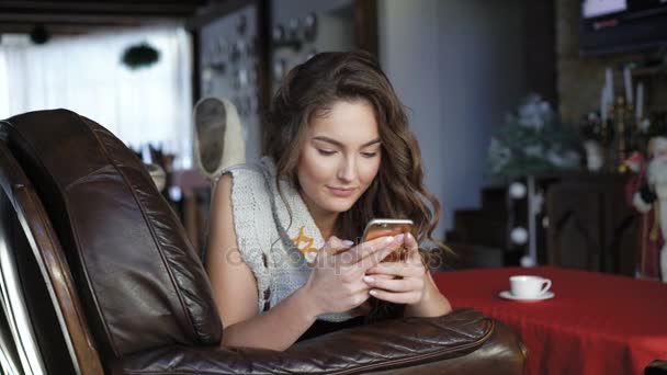 Bella ragazza rilassante sul divano in pelle e utilizzando il telefono cellulare 4K — Video Stock