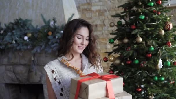 Ευτυχισμένος κορίτσι κρατώντας τα δώρα Χριστουγέννων και το ψάχνει μέσα από το παράθυρο 4k — Αρχείο Βίντεο
