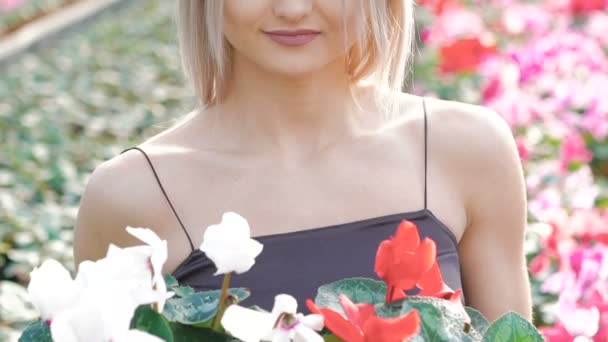 Jolie blonde sentant les fleurs et souriant à la caméra. Doucement. — Video