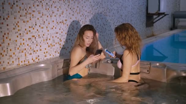 Meninas bonitas descansando em jacuzzi e usando a tecnologia. 4K — Vídeo de Stock
