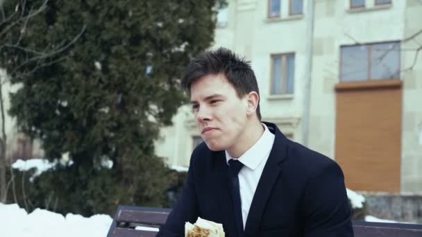 Young businessman sitting on a bench eating at fast food. 4k — Stock Video