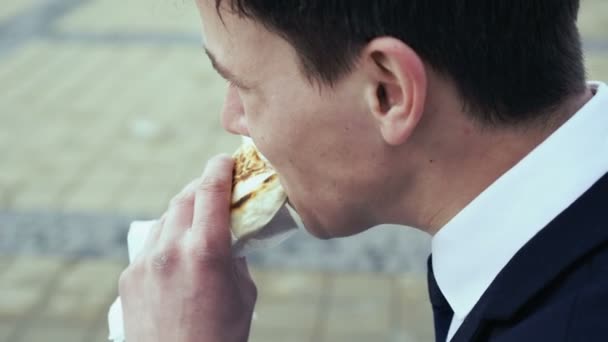 Молодой бизнесмен сидит на скамейке и ест фаст-фуд. 4k — стоковое видео